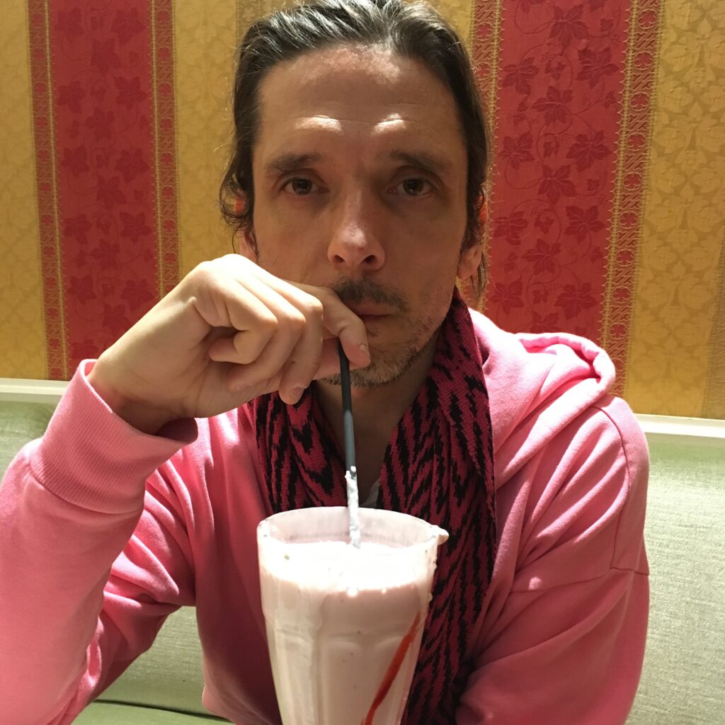 Mand iført lyserød hættetrøje og torklæde drikker en milkshake