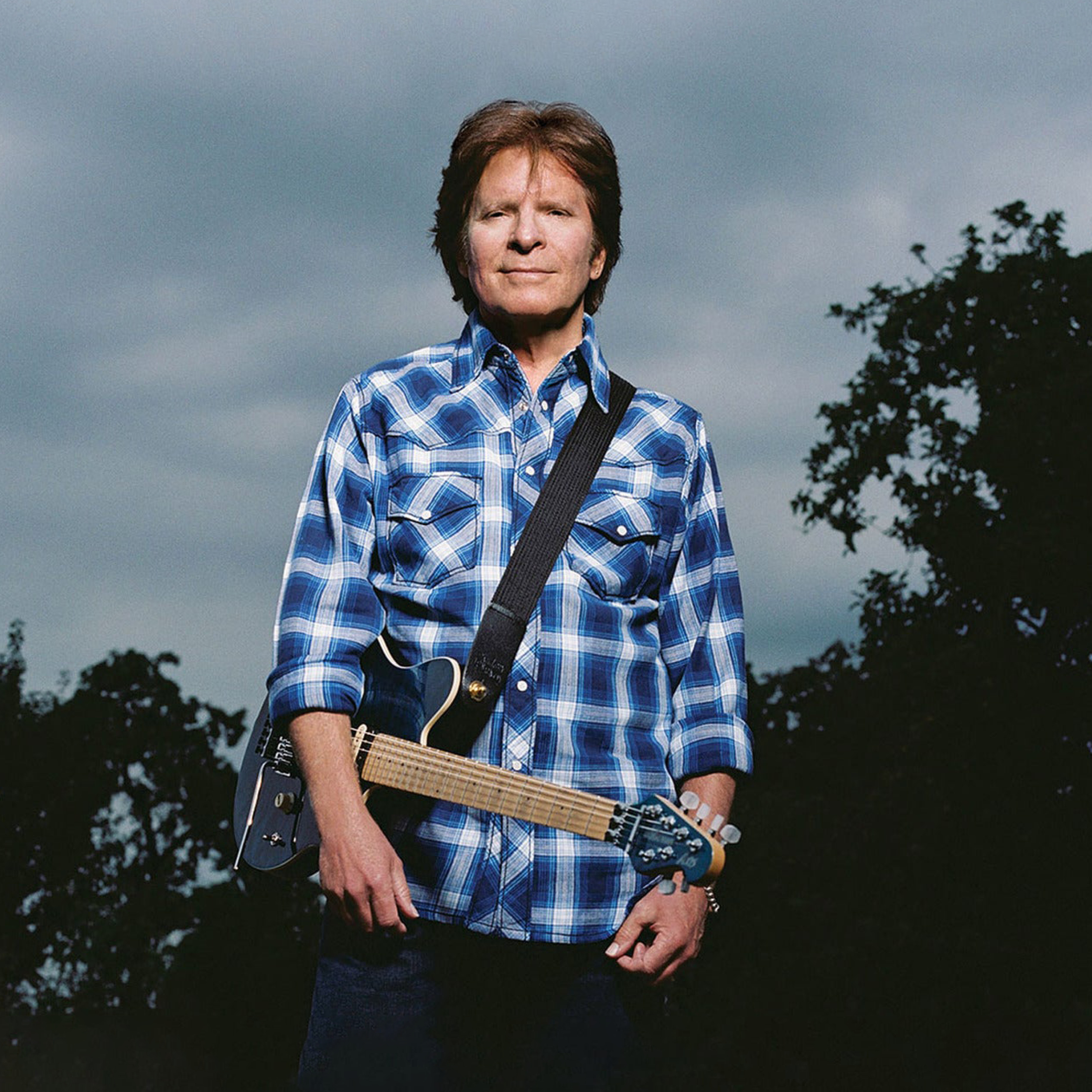 Billede af John Fogerty, iført blå skjorte med guitar