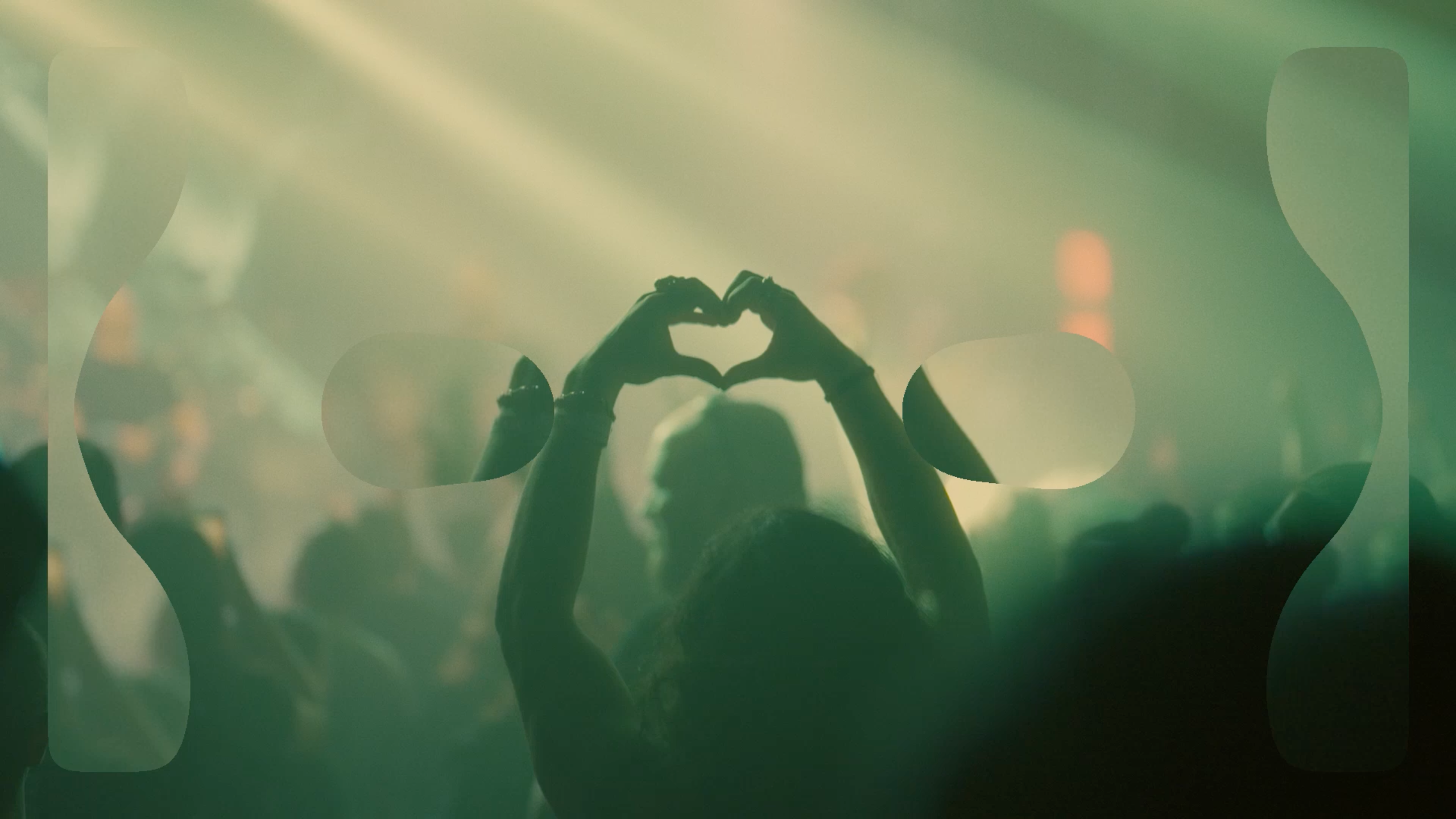 Silhuet af koncertgæst der former et hjerte med hænderne i grønt scenelys med Heartland-grafik i forgrunden.