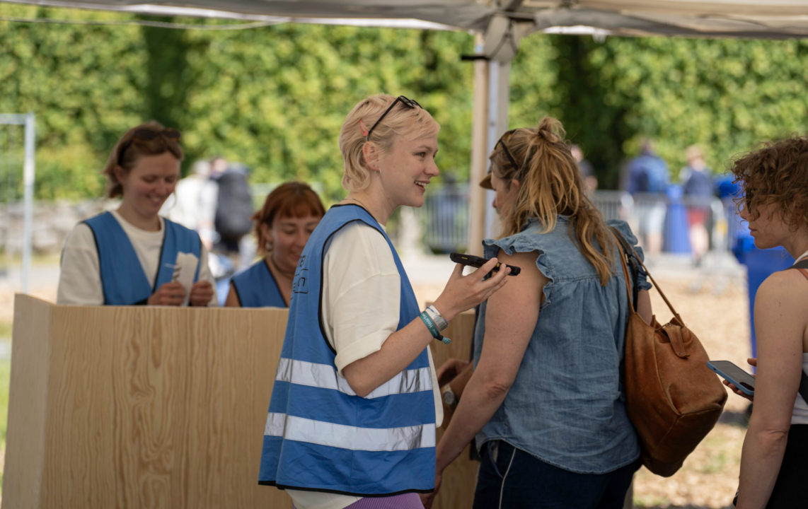 Smilende frivillige i blå refleksveste scanner billetter og byder gæster velkommen ved indgangen til Heartland Festival.
