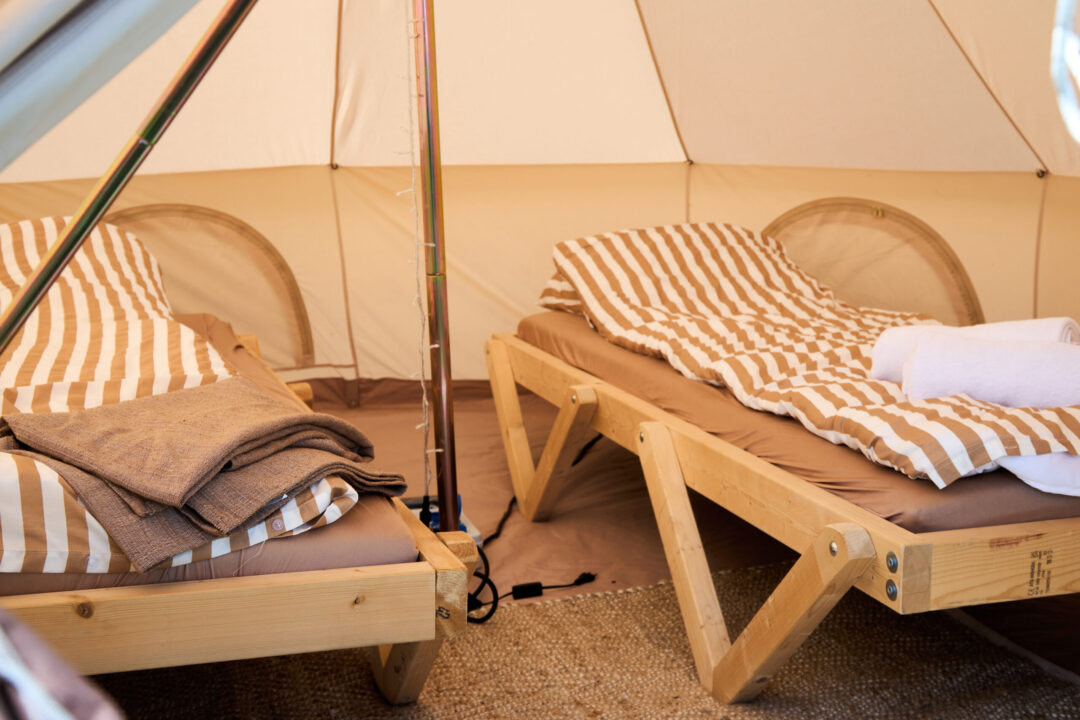 Et kig ind i et glampingtelt, hvor der står to senge med dyner og håndklæder