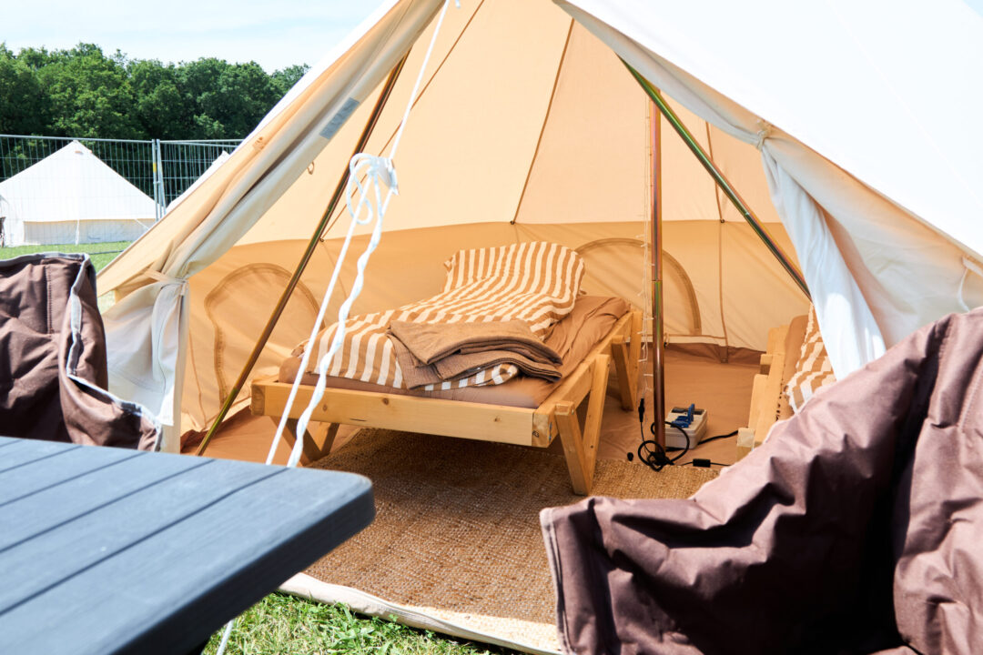 Et kig ind i et glampingtelt, hvor der står to senge med dyner og håndklæder