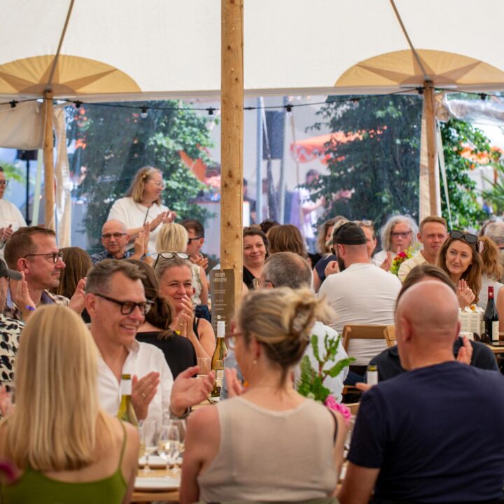 Gæster sidder og hygger sig og spiser/drikker inde under et stort åbent telt.