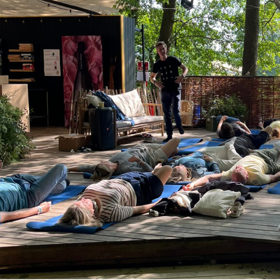 En lille flok mennesker som ligger på underlag og laver øvelser ude i skoven.