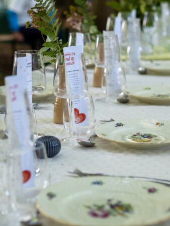 Flot opdækket langbord med hvid dug og blomsterdetaljeret porcelænstallerkener.