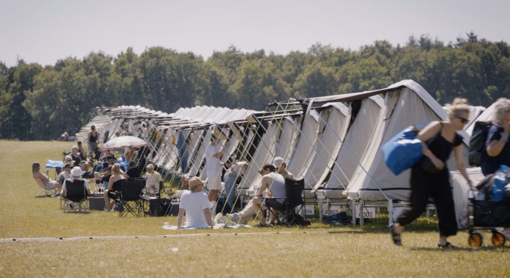 Flere grå tenthouses står på række, og en flok mennesker sidder foran og hygger sig.