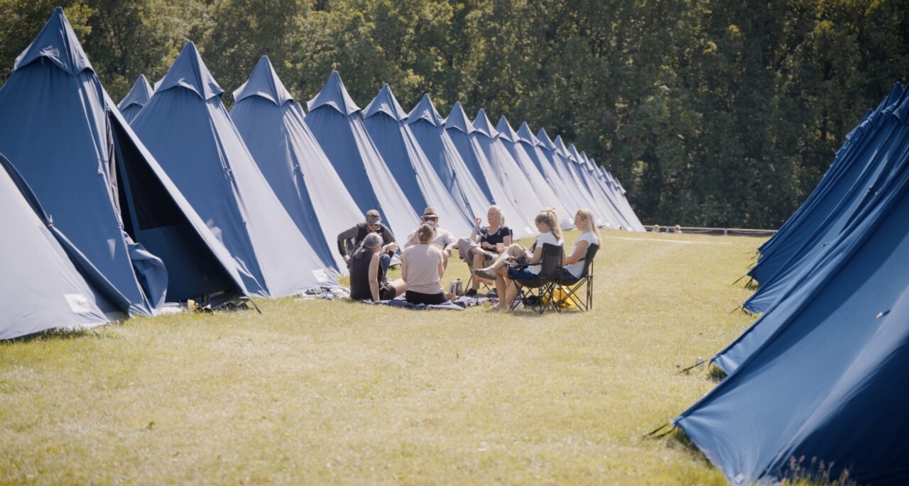 Tipi telte på række med en flok mennesker foran der hygger sig.