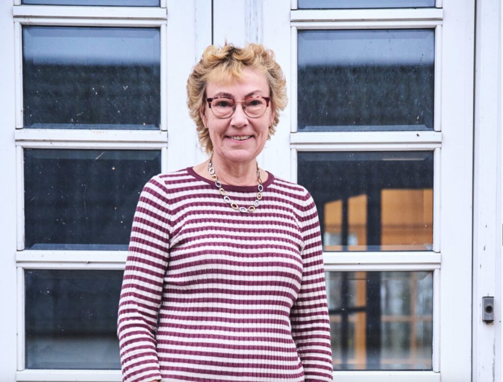 Sød kvinde i en stribet bluse foran sit hus.