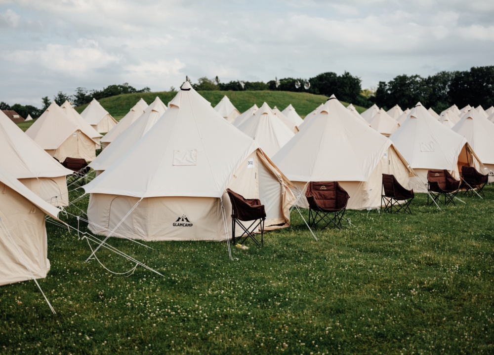 Glampingtelte på række på græsplæne med skov og blå himmel i baggrunden