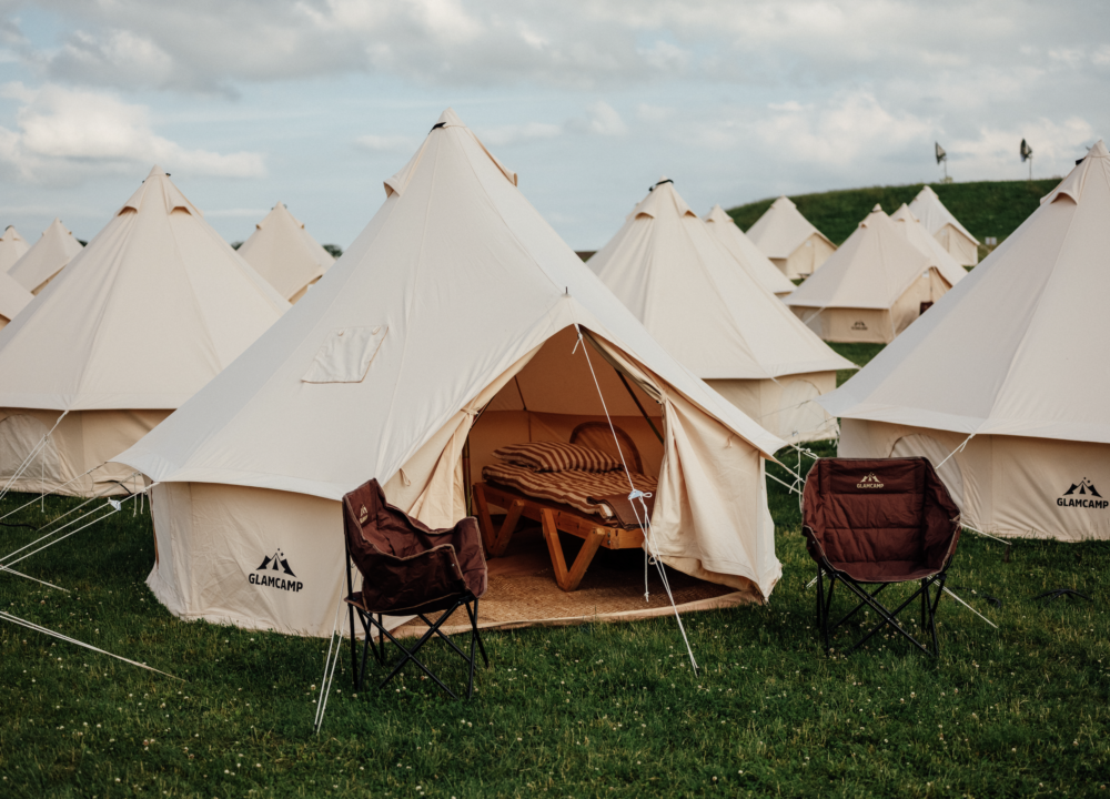 Et åbent glampingtelt på grøn græsplæne med blå himmel i baggrunden