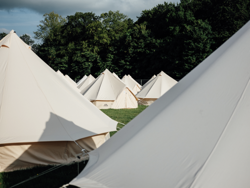 Glampingtelte på række på græsplæne med skov og blå himmel i baggrunden