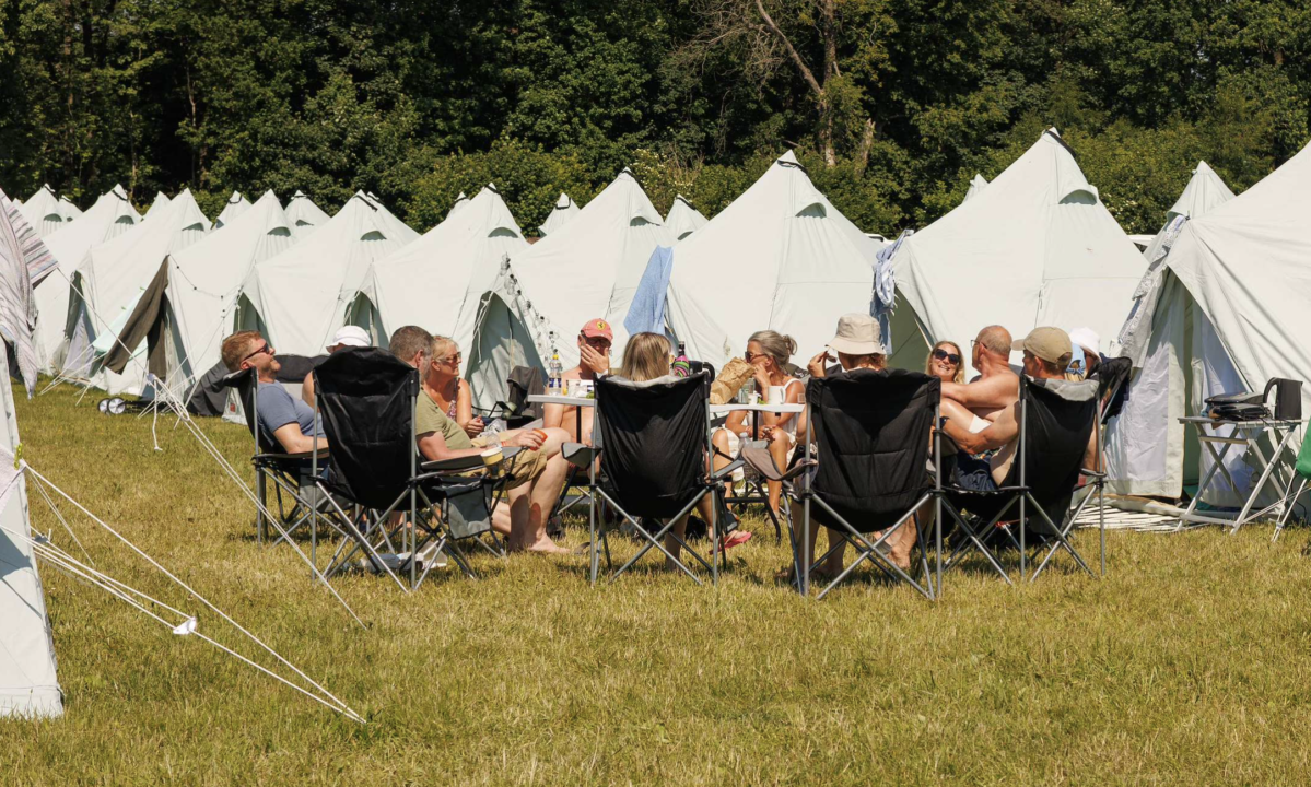 Festivalgæster der sidder ude foran deres tipitelte i campingstole og varmer op til Heartland Festival