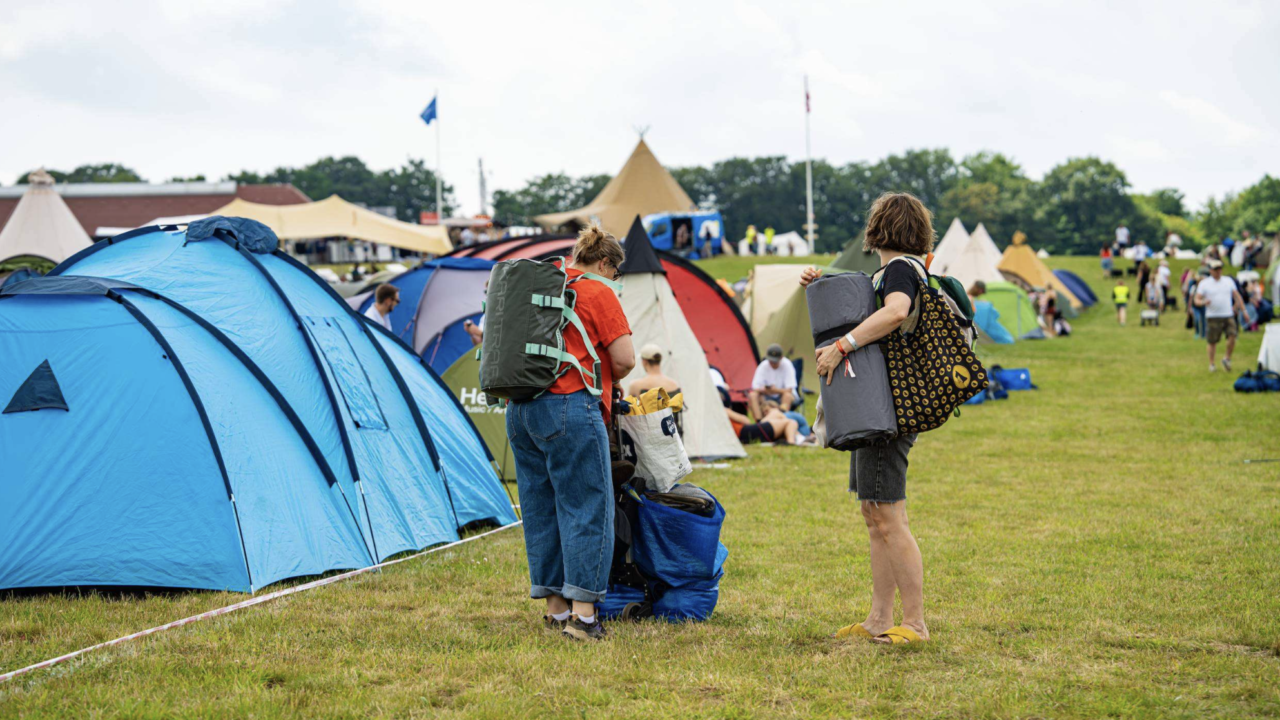Festivalgæster går med campinggrej på ryggen på campingområdet