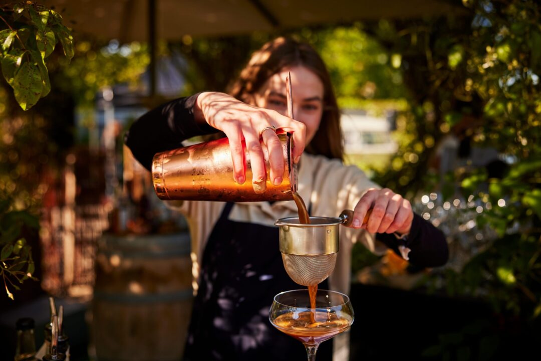 Bartender der hælder en drink op gennem en si.