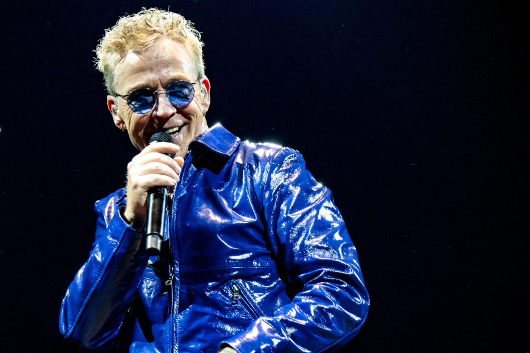 Thomas Helmig i blåt outfit og blå solbriller med en mikrofon i hånden